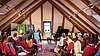 Ein Dachgeschoßsaal mit Holzbalken, Publikum schaut auf Flügel und zwei Redner vorne.