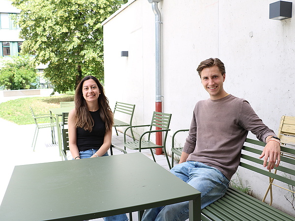 Junge Frau und junger Mann sitzen an einem Tisch auf einer Gartenterrasse.