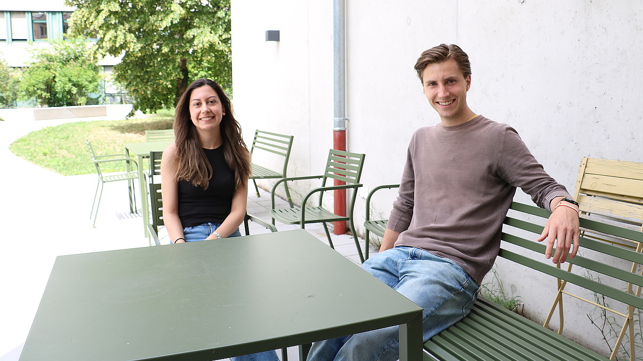 Junge Frau und junger Mann sitzen an einem Tisch auf einer Gartenterrasse.