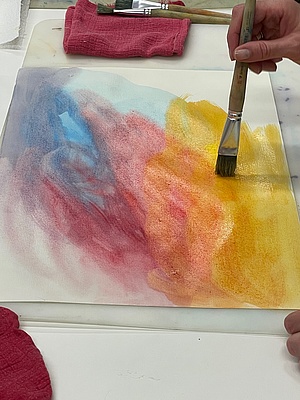 Hand mit Pinsel, blau-rot-orange-gelbe Farbflächen auf Papier (Aquarell)