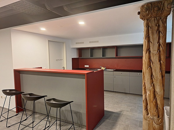 Theke einer Bar in einem Partykeller, rechts neben der Bar eine alte Säule aus Holz, während die restliche Einrichtung modern und nüchtern ist