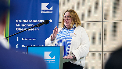 Auf dem Foto sieht man Claudia Meijering, wie sie an einem Rednerpult steht und ihre Rede hält. Dahinter ein Banner mit der Aufschrift "Studierendenwerk München Oberbayern". 