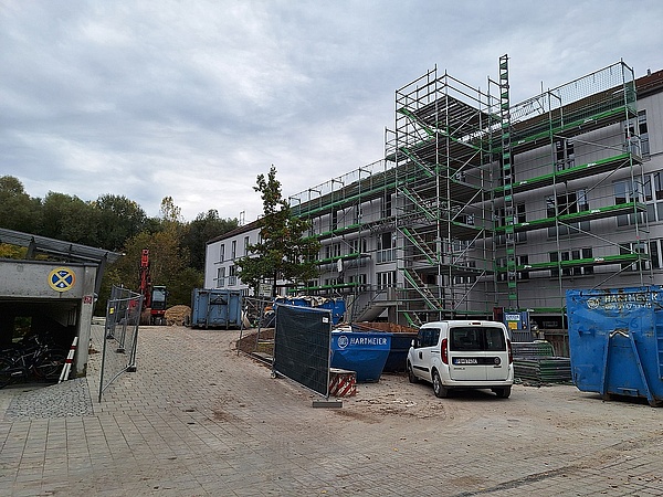 Eingerüstetes Wohnhaus, davor Container und Autos