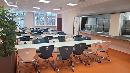 Das Bild zeigt den Innenraum des neuen StuBistros. In der Mitte sind mehrere Tische und Stühle. Im Hintergrund ist eine Essensausgabe erkennbar. 