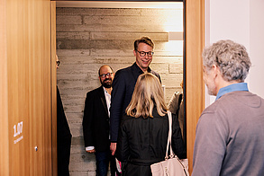 Eröffnungsfeier der Inklusionswohnanlage Auf dem Foto sieht man mehrere Personen, die um eine geöffnete Tür herum stehen. Auf dem Bild auch Markus Blume, der Bayerische Staatsminister für Wissenschaft und Kunst.