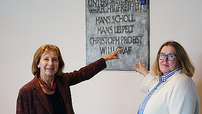 Auf dem Bild sieht man eine Gedenktafel, auf der die Namen der Mitglieder der Weißen Rose stehen. Davor Hildegard Kronawitter von der Weiße-Rose-Stiftung sowie Claudia Meijering, Geschäftsführerin des Studierendenwerks München Oberbayern.