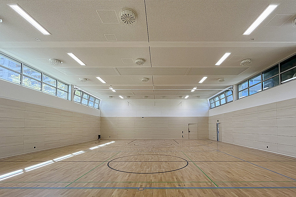 Leere Sporthalle, Fußboden helles Holz, Sonne scheint durch die Fensterluken