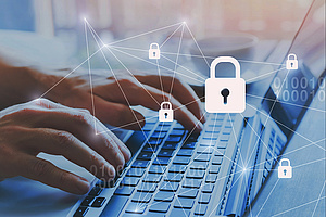 Nahaufnahme von zwei Händen, die auf einer Laptop-Tastatur tippen. Das Bild ist mit einer digitalen Grafik zum Thema Cybersicherheit überlagert, die ein weißes Netzwerk aus verbundenen Linien, mehrere kleine Vorhängeschloss-Symbole, ein großes zentrales Vorhängeschloss sowie schwach erkennbare Binärcode-Sequenzen zeigt.