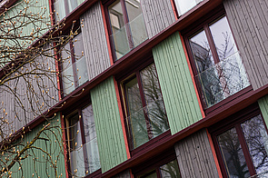 Holzfassade mit abwechselnd dunkelgrün und anthrazitfarben angestrichenen Außenwandelementen, bodentiefe Fenster
