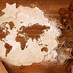 Das Bild zeigt einen ausgerollten Teig, der mit Mehl bestäubt ist. Im Teig sind verschiedene Formen ausgestochen, sodass das Bild an die Weltkarte erinnert. Rechts daneben liegt eine Sternen-Ausstecherform. Im linken Eck außerdem ein Stern, der aus dem Teig ausgestanzt wurde.