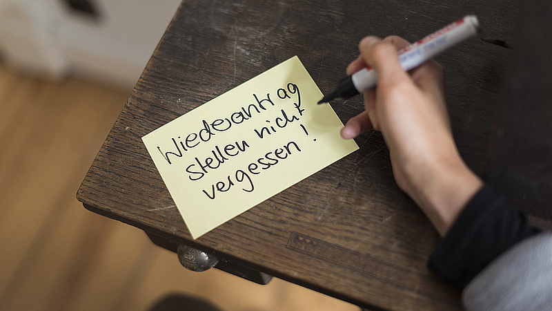 Jemand schreibt "Wiederantrag stellen nicht vergessen" auf eine Haftnotiz