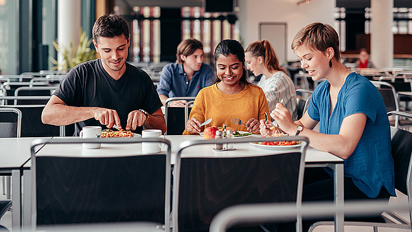 Drei Studiernede sitzen an einem Tisch in der Mensa und essen. 