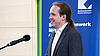 Rede von Dr. Sindre W. Haugland zur Wiedereröffnung der Hans-Scholl-Halle Auf dem Foto sieht man Dr. Sindre W. Haugland, Vorstand Studentenstadt München e.V, wie er an einem Rednerpult steht und ihre Rede hält. Dahinter ein Banner mit der Aufschrift "Studierendenwerk München Oberbayern".