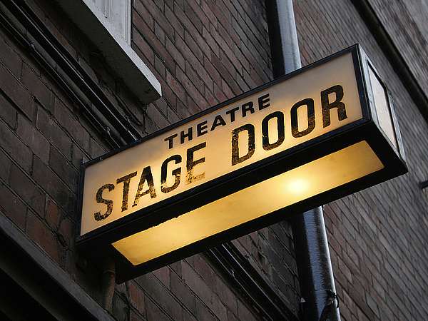 Symbolbild für Kultur: Backsteinhaus mit einem leuchtenden Bühnenschild, auf dem "Stage Door" steht.