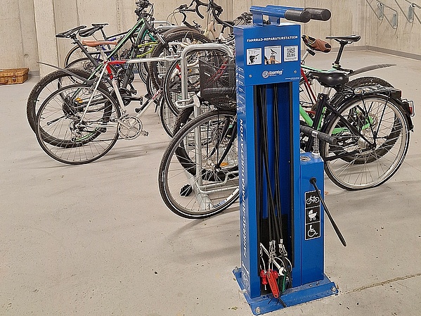 Fahrradkeller, viele Fahrräder nebeneinander auf Fahrradständern, im Vordergrund eine Säule mit Werkzeug