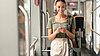 Frau mit Kopfhörern steht in einer Tram und blickt auf ihr Smartphone.
